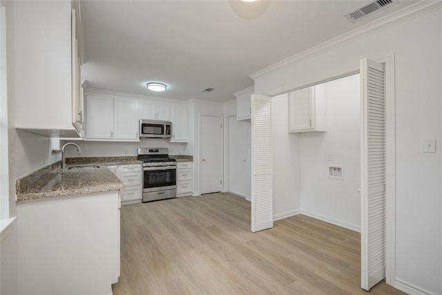110 Spruce St, Lake Jackson, TX 77566 - kitchen featuring appliances with stainless steel finishes, white cabinets, light stone countertops, light wood finished floors, and ornamental molding