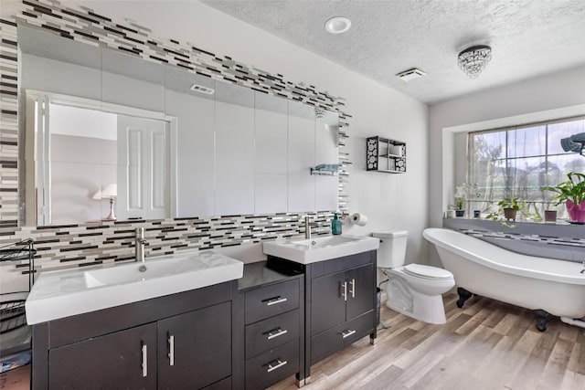 2806 Spring Dusk Ln, Spring, TX 77373 - bathroom with double vanity, tasteful backsplash, wood finished floors, a soaking tub, and a textured ceiling