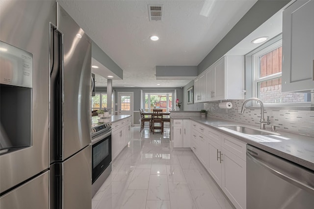12206 Green Glade Dr, Houston, TX 77099 - kitchen featuring appliances with stainless steel finishes, light marble finish floors, white cabinets, a textured ceiling, and decorative backsplash
