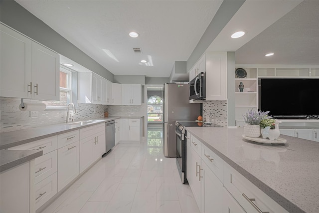 12206 Green Glade Dr, Houston, TX 77099 - kitchen featuring appliances with stainless steel finishes, light stone counters, light marble finish flooring, white cabinets, and recessed lighting