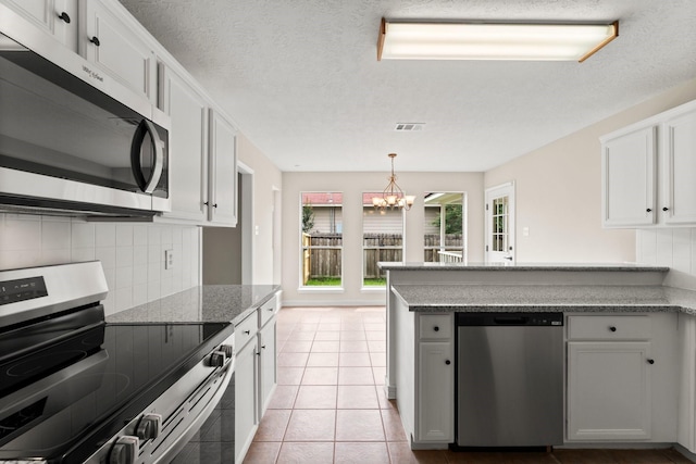 519 Tallow Dr, Conroe, TX 77385 - kitchen featuring stainless steel appliances, a chandelier, decorative backsplash, a peninsula, and white cabinetry
