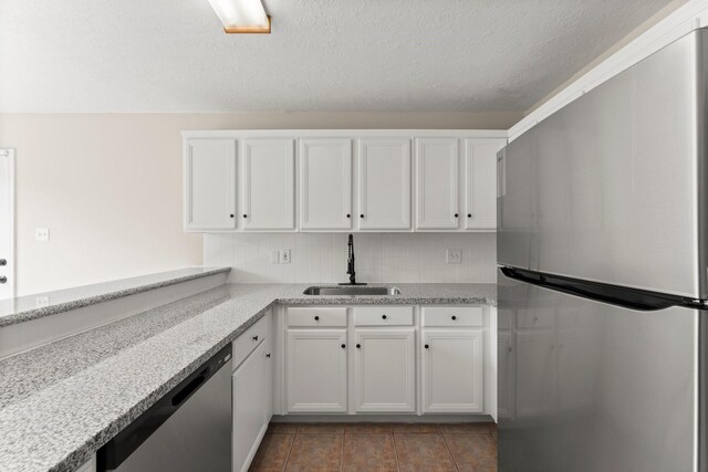 519 Tallow Dr, Conroe, TX 77385 - kitchen featuring appliances with stainless steel finishes, white cabinetry, light stone counters, tile patterned floors, and a textured ceiling