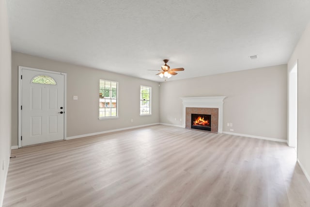 519 Tallow Dr, Conroe, TX 77385 - unfurnished living room with light wood finished floors, a ceiling fan, a tile fireplace, and a textured ceiling
