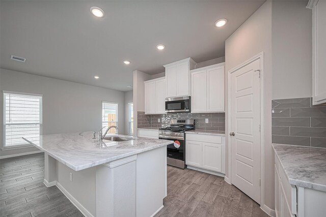 24711 Sonora Crescent Cir, Huffman, TX 77336 - kitchen with appliances with stainless steel finishes, light wood-style floors, decorative backsplash, a center island with sink, and recessed lighting