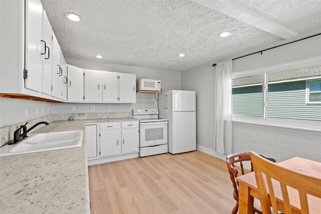 4034 Reeves Dr, Galveston, TX 77554 - kitchen with white appliances, a textured ceiling, light countertops, white cabinets, and light wood-style floors