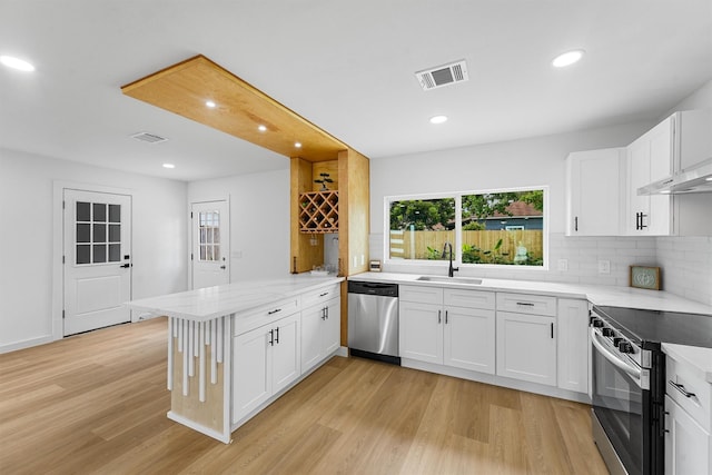 3303 Dartmouth Dr, Pasadena, TX 77503 - kitchen with stainless steel appliances, a peninsula, light wood-style flooring, backsplash, and white cabinetry