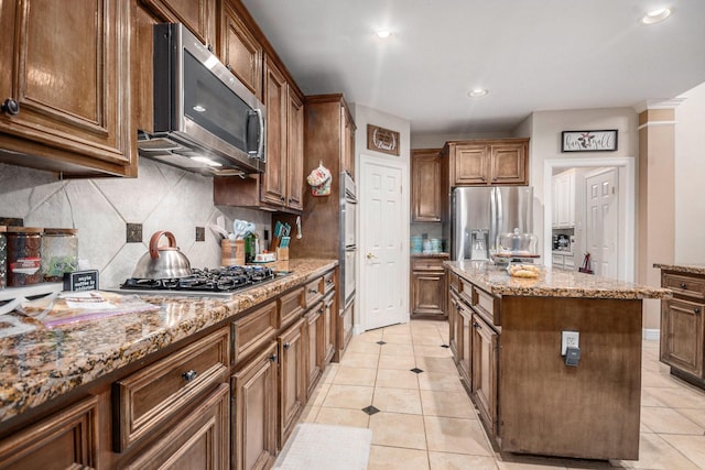 305 Pinnacle Cove Ct, League City, TX 77573 - kitchen featuring appliances with stainless steel finishes, a kitchen island, light tile patterned floors, backsplash, and light stone countertops