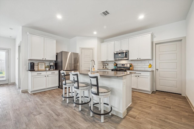 7714 Cattleman Valley Dr, Rosharon, TX 77583 - kitchen featuring stainless steel appliances, tasteful backsplash, a kitchen bar, light wood-style flooring, and a kitchen island with sink