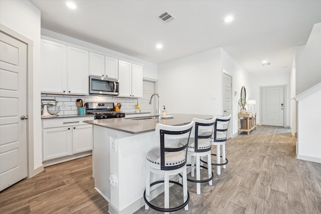 7714 Cattleman Valley Dr, Rosharon, TX 77583 - kitchen with appliances with stainless steel finishes, a center island with sink, light wood-type flooring, backsplash, and a breakfast bar area