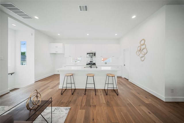 1124 Hogan St, Houston, TX 77009 - kitchen with appliances with stainless steel finishes, white cabinetry, a center island with sink, light wood-type flooring, and a breakfast bar