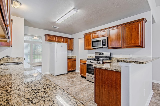 11230 Chelsea Oak St, Houston, TX 77065 - kitchen with stainless steel appliances, a peninsula, light stone countertops, a textured ceiling, and brown cabinetry