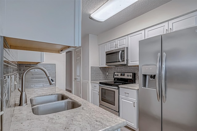 8427 Ariel St, Houston, TX 77074 - kitchen featuring stainless steel appliances, backsplash, white cabinetry, light stone counters, and a textured ceiling