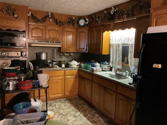 404 Svoboda St, Yoakum, TX 77995 - kitchen with black appliances, under cabinet range hood, brown cabinetry, and light tile patterned floors