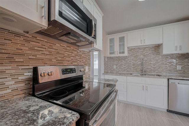 3930 Daphne St, Houston, TX 77021 - kitchen with appliances with stainless steel finishes, backsplash, white cabinetry, glass insert cabinets, and light stone countertops
