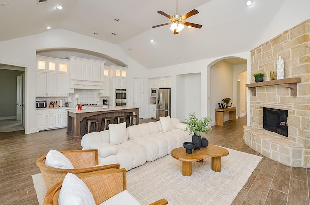 27522 Blackstone Canyon Ln, Katy, TX 77494 - living room featuring a ceiling fan, arched walkways, dark wood-type flooring, a stone fireplace, and high vaulted ceiling