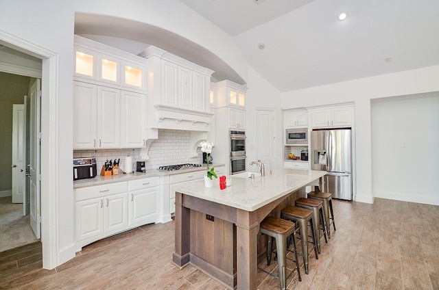 27522 Blackstone Canyon Ln, Katy, TX 77494 - kitchen featuring appliances with stainless steel finishes, white cabinetry, backsplash, lofted ceiling, and a breakfast bar
