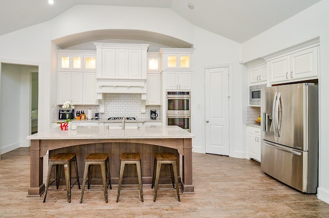 27522 Blackstone Canyon Ln, Katy, TX 77494 - kitchen featuring appliances with stainless steel finishes, vaulted ceiling, white cabinetry, light stone countertops, and glass insert cabinets