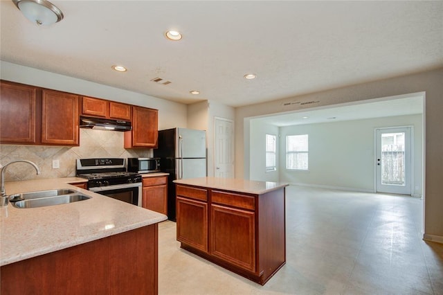 2666 Skyview Knoll Ct, Houston, TX 77047 - kitchen with appliances with stainless steel finishes, under cabinet range hood, tasteful backsplash, brown cabinetry, and a center island