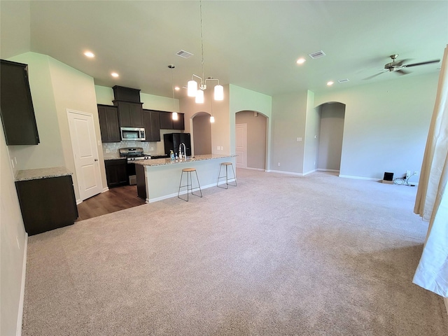 2320 Cedar Place Dr, Conroe, TX 77306 - kitchen with appliances with stainless steel finishes, arched walkways, light carpet, open floor plan, and a center island with sink