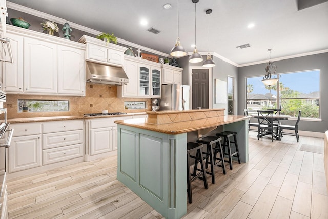 3038 S Island Dr, Seabrook, TX 77586 - kitchen featuring under cabinet range hood, stainless steel appliances, a kitchen island, white cabinets, and light wood finished floors
