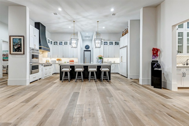 4622 Banning Dr, Houston, TX 77027 - kitchen with wall chimney range hood, decorative backsplash, a breakfast bar, light countertops, and white cabinetry