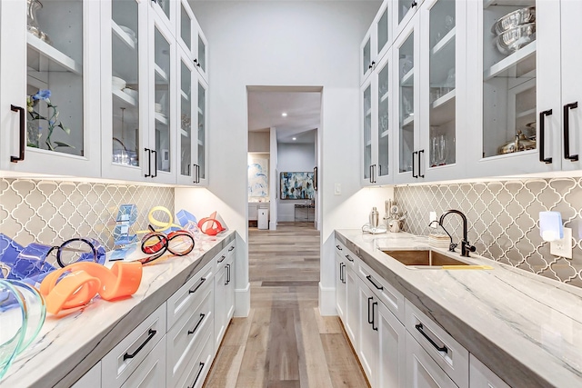 4622 Banning Dr, Houston, TX 77027 - kitchen with light wood-type flooring, light stone countertops, glass insert cabinets, and backsplash