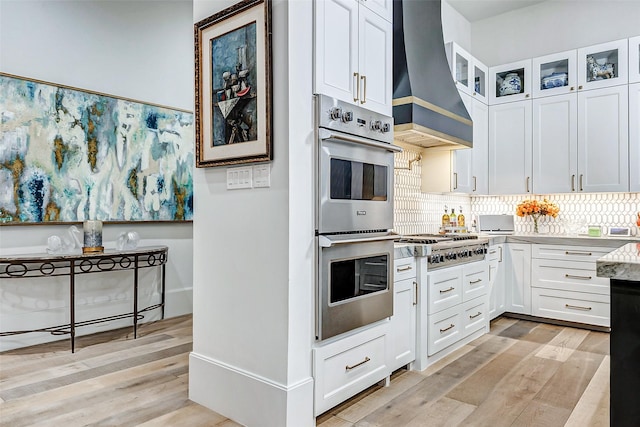 4622 Banning Dr, Houston, TX 77027 - kitchen featuring custom exhaust hood, stainless steel appliances, light wood-style floors, white cabinets, and glass insert cabinets