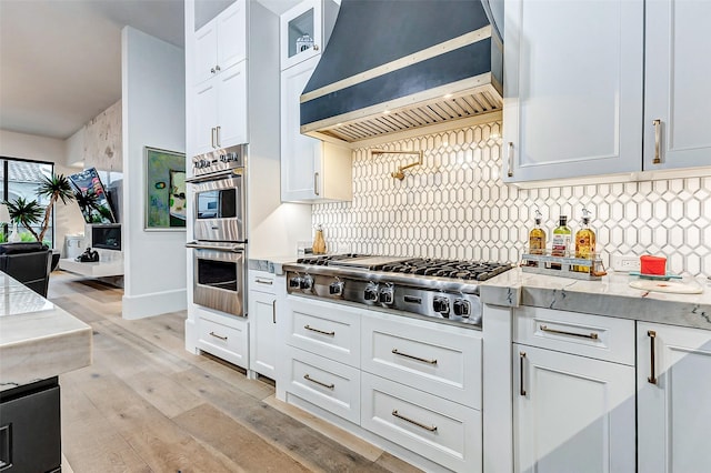 4622 Banning Dr, Houston, TX 77027 - kitchen featuring custom exhaust hood, appliances with stainless steel finishes, tasteful backsplash, light wood finished floors, and white cabinetry