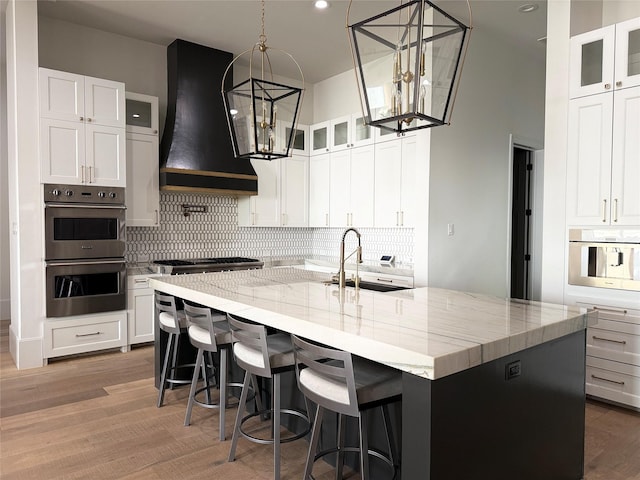 4622 Banning Dr, Houston, TX 77027 - kitchen featuring extractor fan, appliances with stainless steel finishes, a large island with sink, light stone countertops, and decorative backsplash