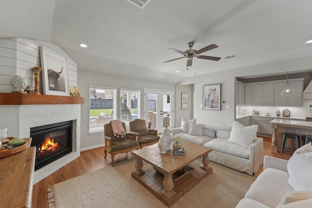 2307 Hagerman Rd, Conroe, TX 77384 - living area with ceiling fan, vaulted ceiling, light wood-type flooring, a large fireplace, and a textured ceiling