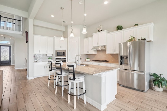 29446 Westhope Dr, Spring, TX 77386 - kitchen featuring stainless steel appliances, under cabinet range hood, light wood finished floors, an island with sink, and white cabinets