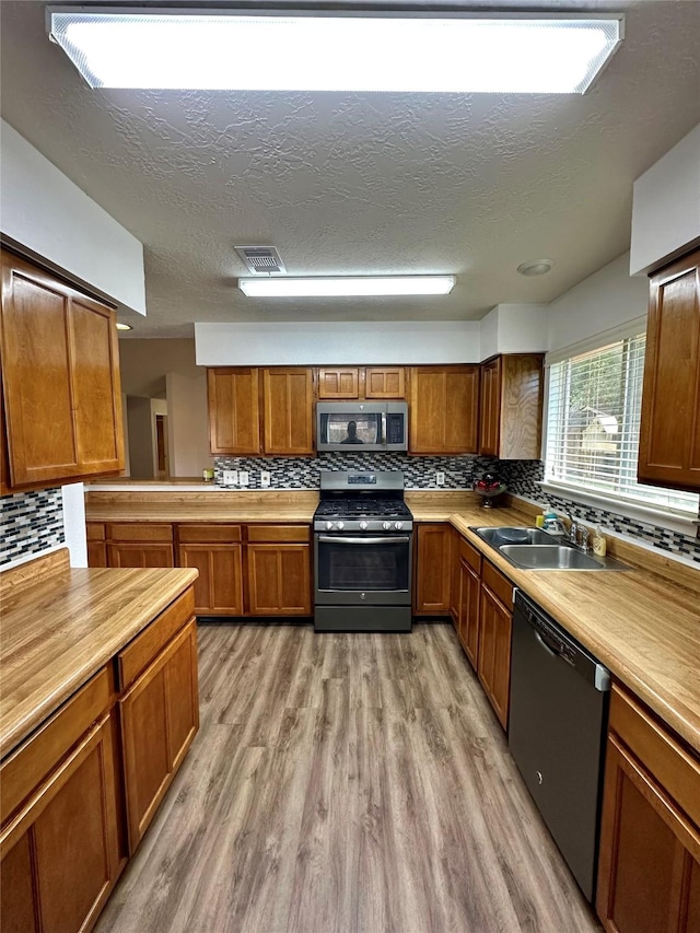 7254 Sonnet Glen Ln, Houston, TX 77095 - kitchen featuring stainless steel appliances, brown cabinetry, backsplash, light wood finished floors, and a textured ceiling