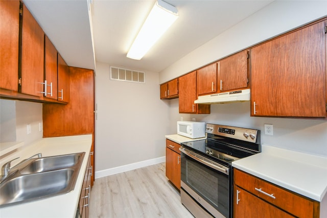 12905 Woodforest Blvd Unit 202, Houston, TX 77015 - kitchen with stainless steel electric stove, under cabinet range hood, white microwave, brown cabinets, and light wood finished floors