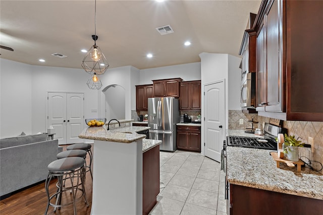 4202 Carnes Ct S, College Station, TX 77845 - kitchen with stainless steel appliances, decorative backsplash, a kitchen bar, an island with sink, and light stone countertops