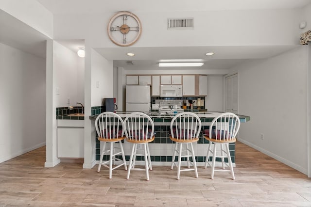 12800 Melville Dr Unit B207, Montgomery, TX 77356 - kitchen featuring a breakfast bar area, white appliances, a peninsula, light wood-style flooring, and backsplash