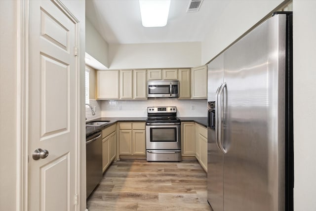 3200 Bellefontaine St Unit 72, Houston, TX 77025 - kitchen featuring appliances with stainless steel finishes, light wood finished floors, decorative backsplash, cream cabinetry, and dark countertops
