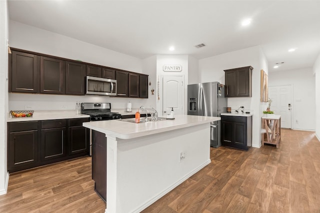 5315 Shady Olive St, Katy, TX 77449 - kitchen featuring wood finished floors, appliances with stainless steel finishes, light countertops, dark brown cabinets, and a kitchen island with sink