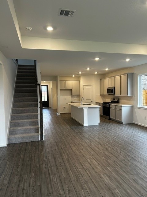 1127 Buffalo Run, Tomball, TX 77375 - kitchen with black range oven, stainless steel microwave, dark wood-style floors, an island with sink, and light countertops