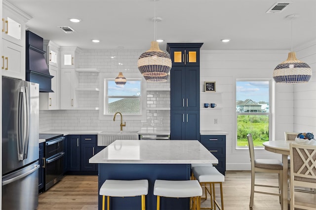210 Galveston St, Crystal Beach, TX 77650 - kitchen with appliances with stainless steel finishes, premium range hood, light wood-type flooring, blue cabinets, and a breakfast bar