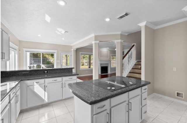 9110 Memorial Creek Dr, Spring, TX 77379 - kitchen with black electric cooktop, a fireplace with flush hearth, ornamental molding, light tile patterned floors, and dark stone counters