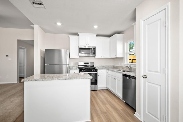 10391 Red Cardinal Dr, Cleveland, TX 77328 - kitchen featuring appliances with stainless steel finishes, a kitchen island, white cabinets, light stone countertops, and light wood finished floors