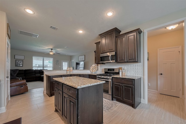 9119 Anna St, Needville, TX 77461 - kitchen featuring appliances with stainless steel finishes, a peninsula, dark brown cabinets, open floor plan, and recessed lighting