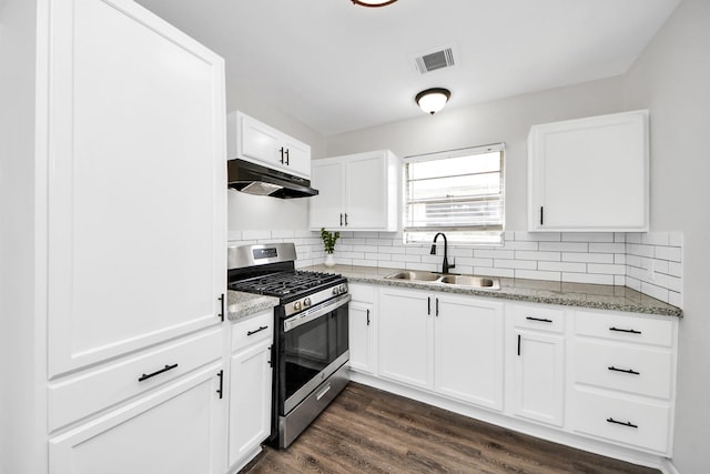 9611 Bertwood St, Houston, TX 77016 - kitchen featuring stainless steel gas stove, under cabinet range hood, backsplash, dark wood finished floors, and white cabinets
