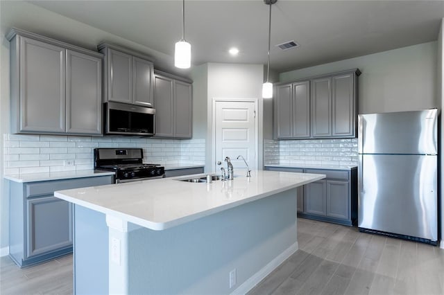 1202 Oak Barrel Run, Richmond, TX 77406 - kitchen featuring appliances with stainless steel finishes, gray cabinets, light wood-style floors, a kitchen island with sink, and decorative backsplash