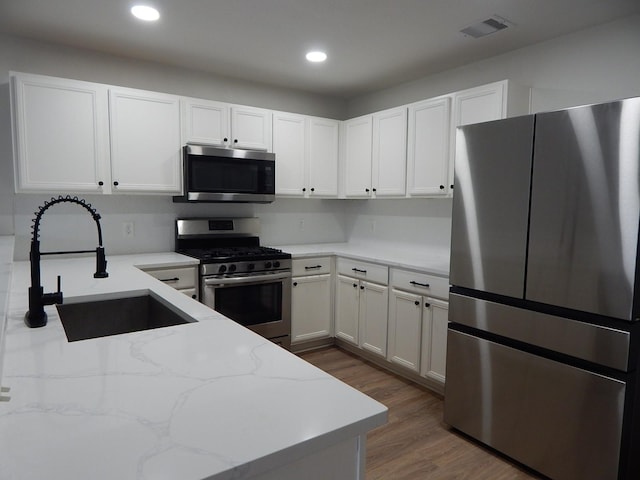 16861 Greenhouse St, Conroe, TX 77385 - kitchen featuring appliances with stainless steel finishes, light stone counters, wood finished floors, white cabinets, and recessed lighting