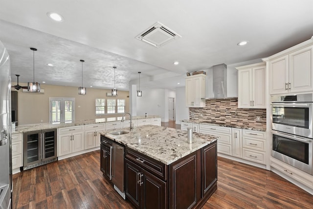 43919 Austin Branch Rd, Hempstead, TX 77445 - kitchen with beverage cooler, wall chimney range hood, double oven, a kitchen island with sink, and dark wood-style floors