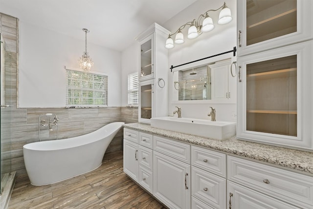 43919 Austin Branch Rd, Hempstead, TX 77445 - bathroom featuring double vanity, a freestanding bath, a chandelier, tile walls, and wood finished floors