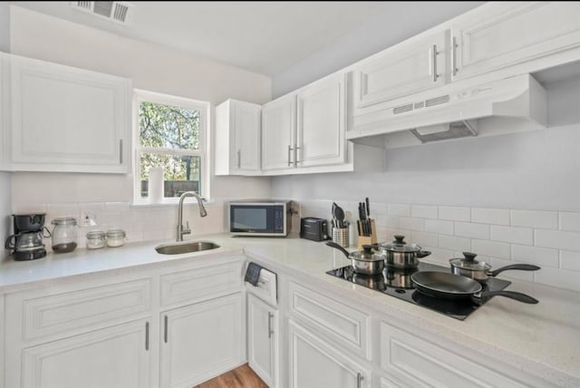 3709 Anita St, Houston, TX 77004 - kitchen with stainless steel microwave, under cabinet range hood, decorative backsplash, and white cabinetry