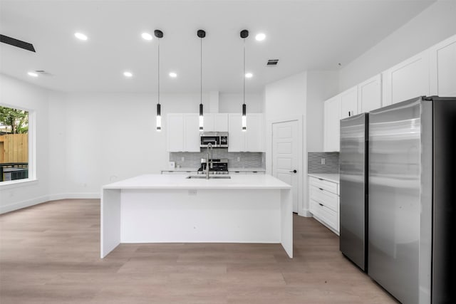 6815 Paris St, Houston, TX 77021 - kitchen featuring appliances with stainless steel finishes, decorative backsplash, light countertops, a kitchen island with sink, and white cabinets
