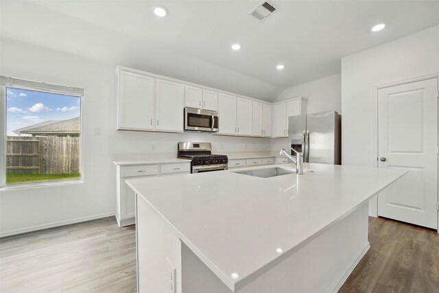 2921 Eden Lake Ln, Katy, TX 77493 - kitchen with appliances with stainless steel finishes, white cabinetry, light wood-style floors, light countertops, and a center island with sink